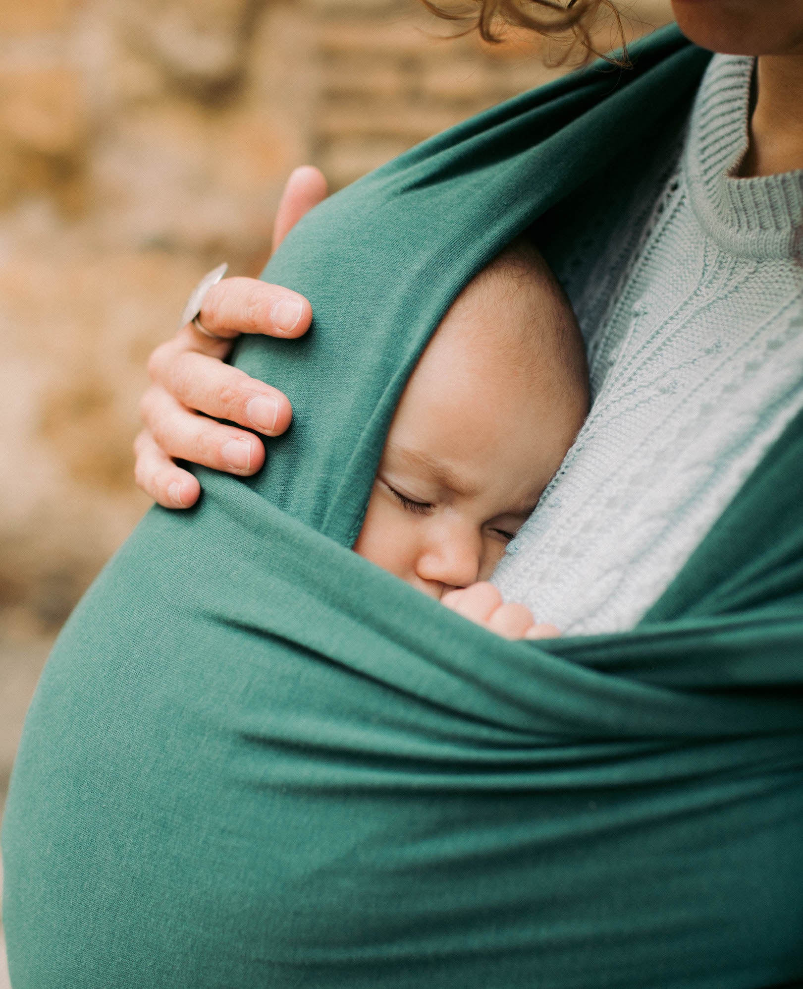 Brown curly haired mother is holding her baby daughter in the front carry in her rainforest serenity wrap.