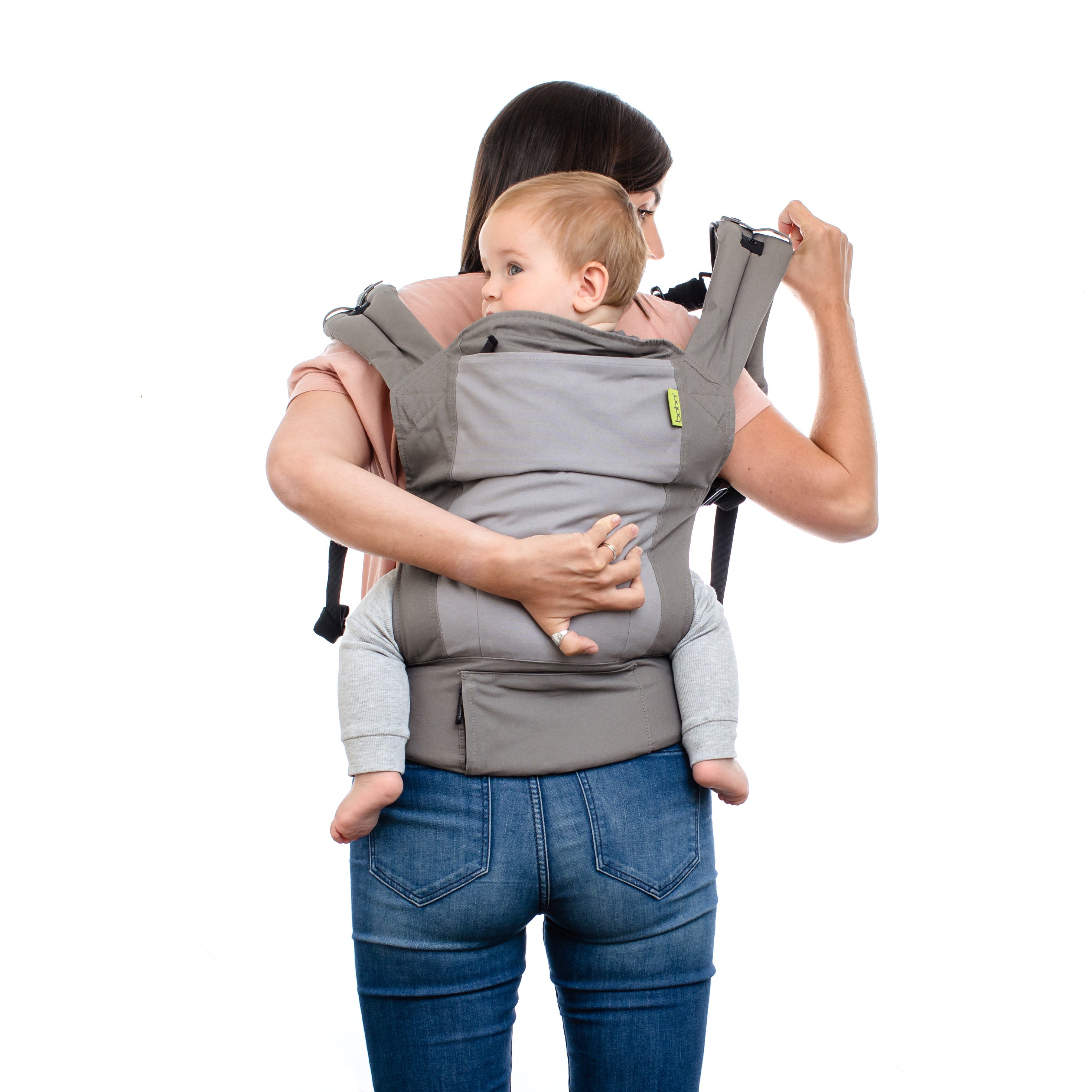 A joyful mama with brown short hair is putting her little boy in the ergonomic and practical back carry in the gray 4gs dusk infant carrier.