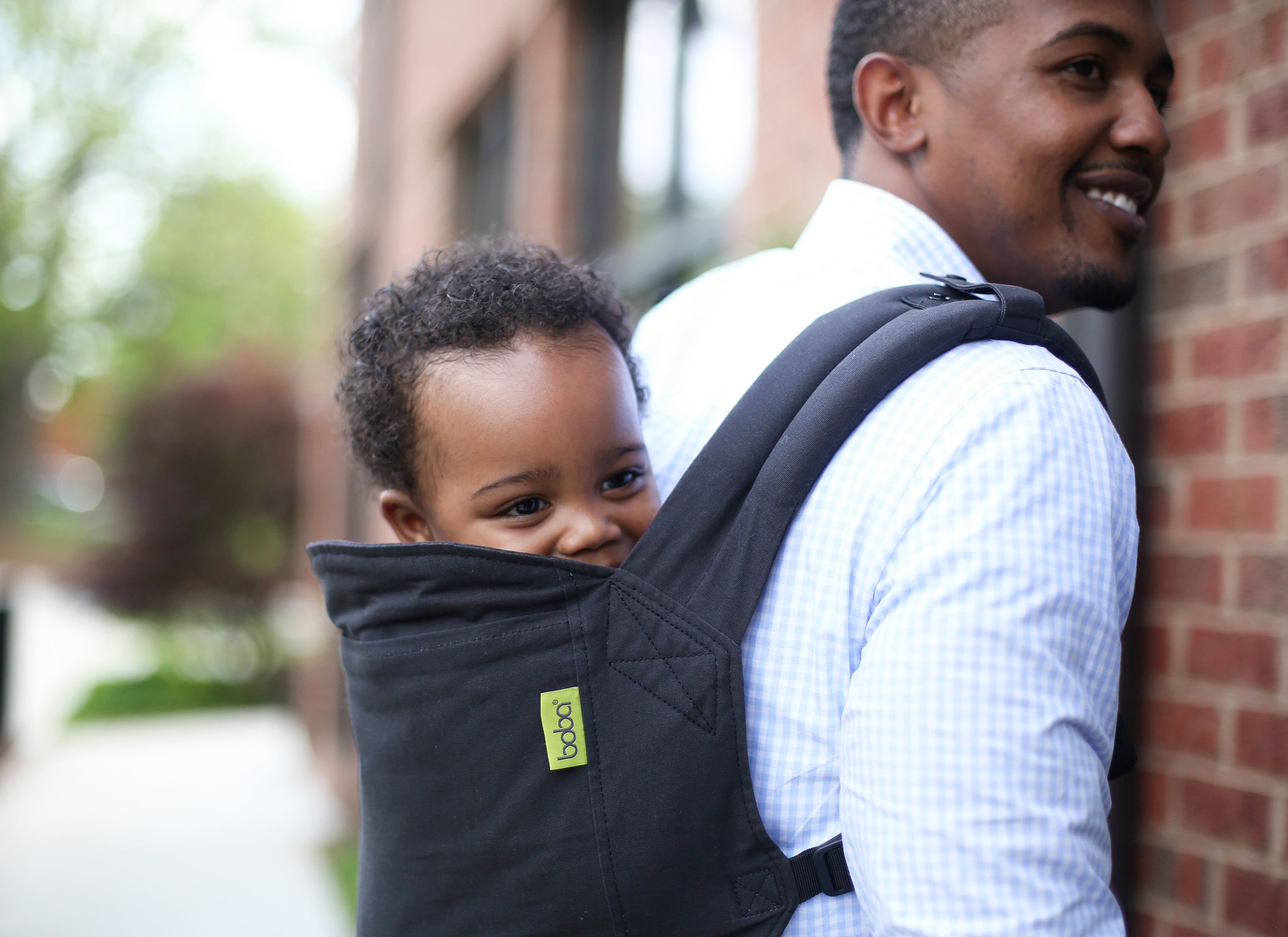 Black dad and son duo are smiling and happy as the father carries his son in the boba 4gs classic carrier in a dark charcoal carrier.