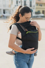 A lightweight, black Boba Air Baby Travel Carrier with padded mesh straps, leg openings, adjustable shoulder straps, and an integrated hood. Compact and self-storing, it fits babies 4-24 months (15+ lbs) and children up to 45 lbs.