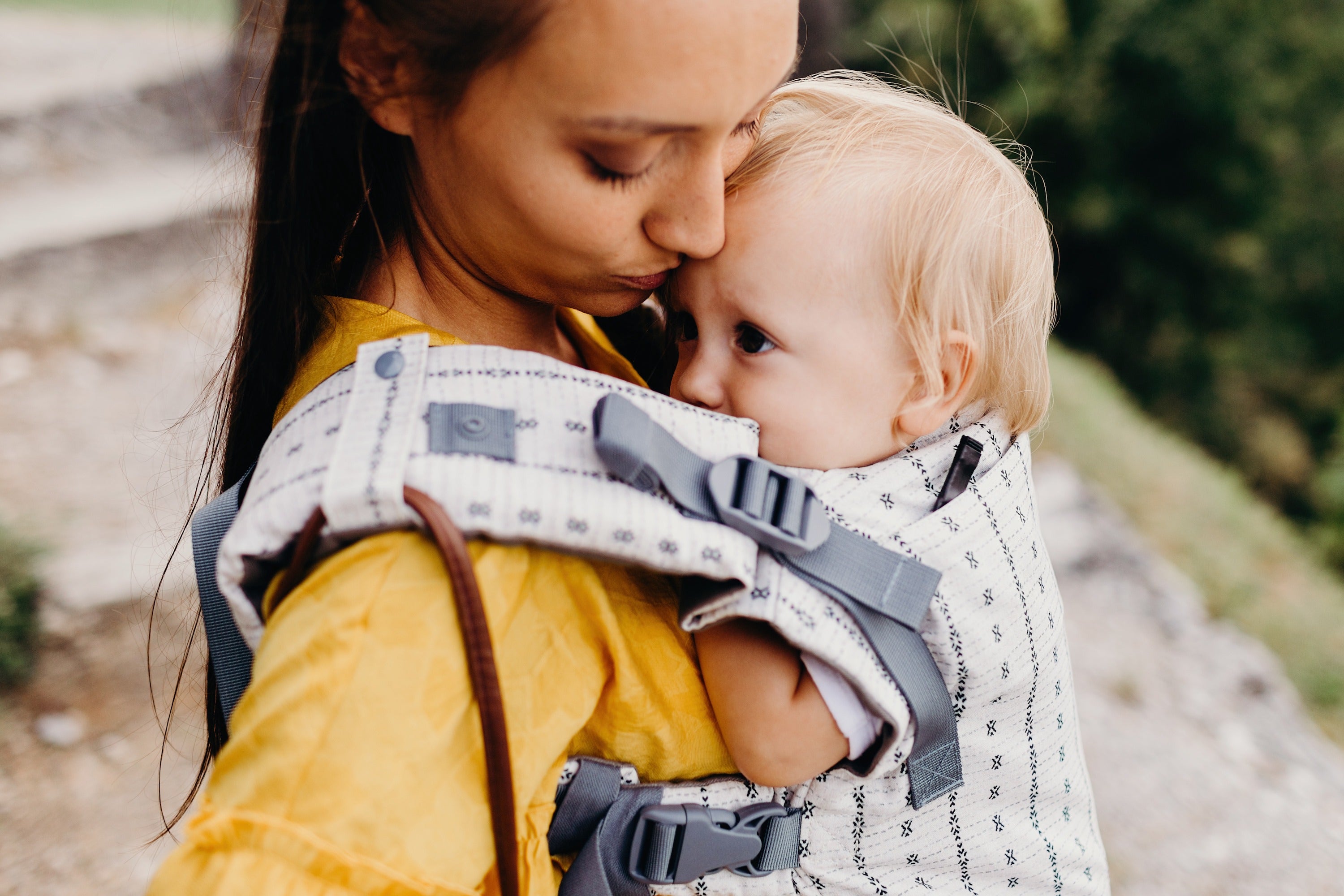 Happy mom kissing her baby's forehead when wearing her little girl in the boba x baby carrier yucca.