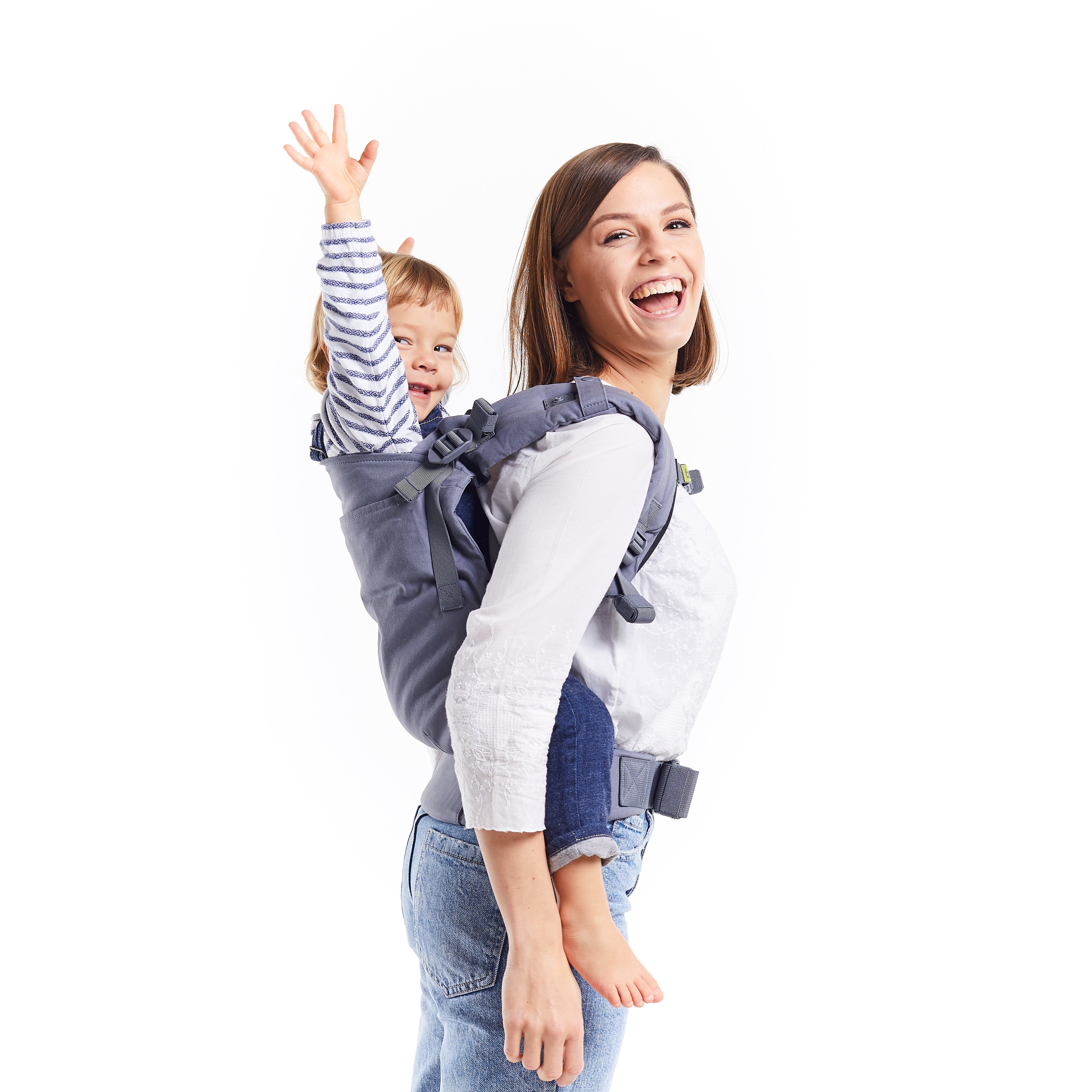 Young brown haired mom is wearing her toddler daughter on her back in the gray boba x baby carrier.