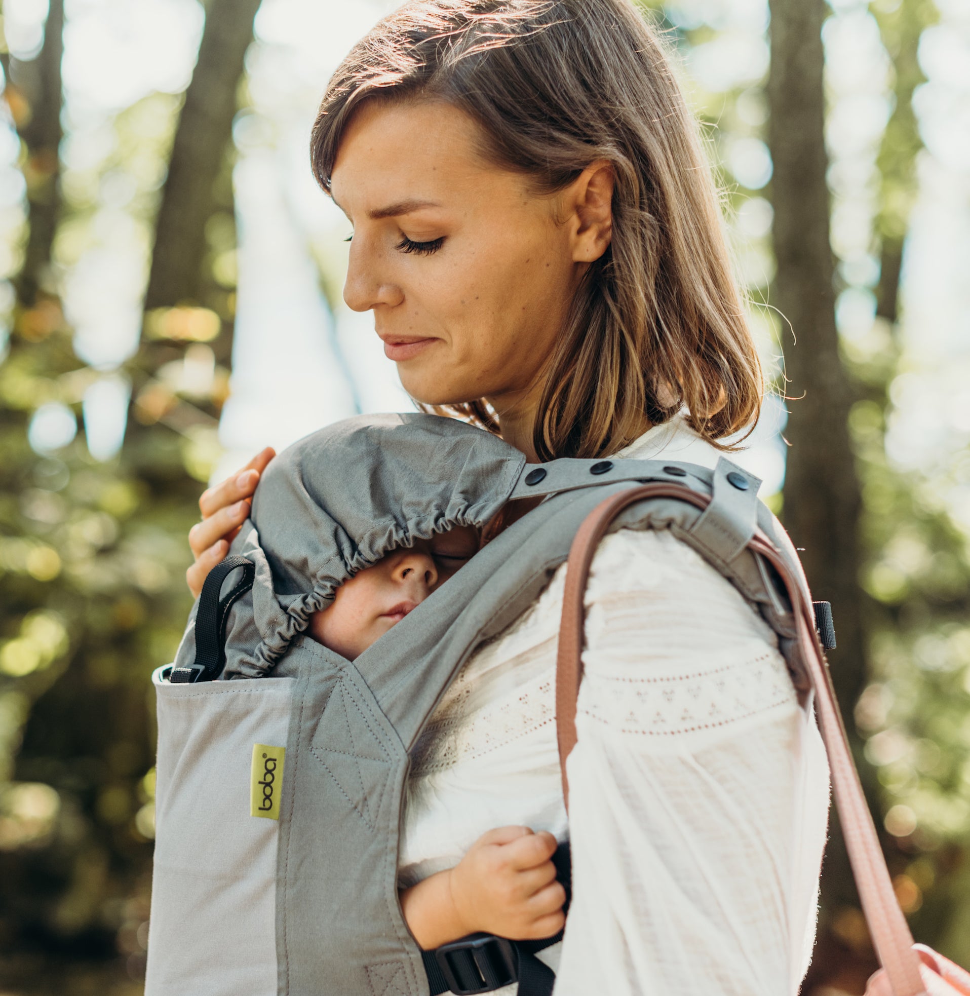 A close up shot of the purse strap and hood in use on the boba classic gray carrier. A mother wearing her sleeping baby son in the front carry.